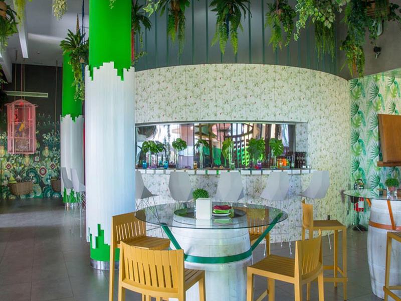 Moderner Innenraum eines Cafés mit runden Tischen, Holzstühlen und grünem Pflanzen-Design.