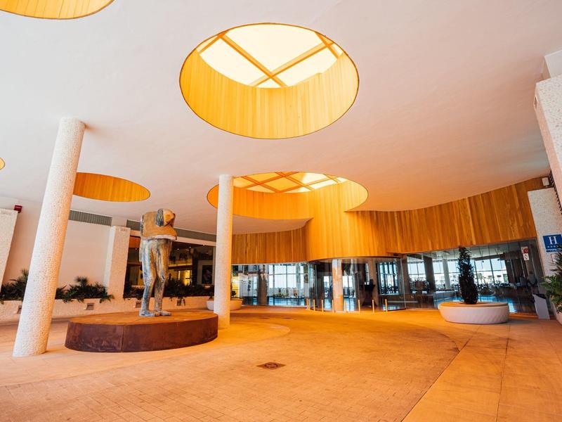 Moderner Hotel-Lobby-Bereich mit runden Deckenfenstern und einer Skulptur in der Mitte.