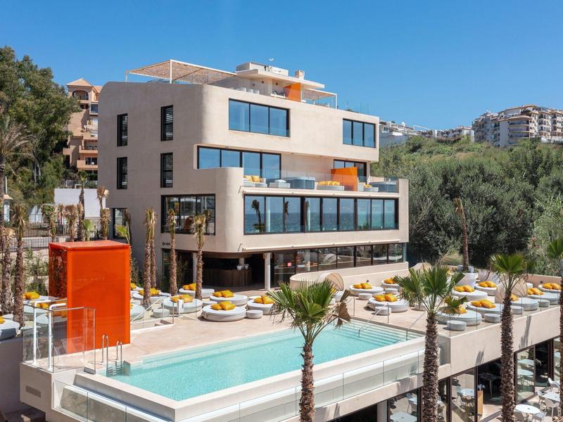 Modernes Hotel mit Pool, Sonnenterrasse und mediterraner Landschaft bei klarem Himmel.