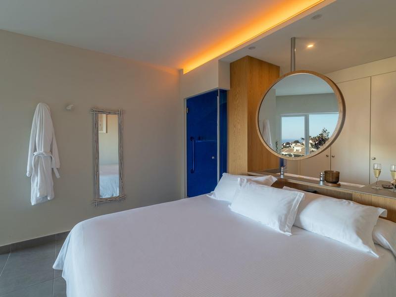 Modernes Hotelzimmer mit großem Bett, rundem Spiegel und indirekter Beleuchtung.