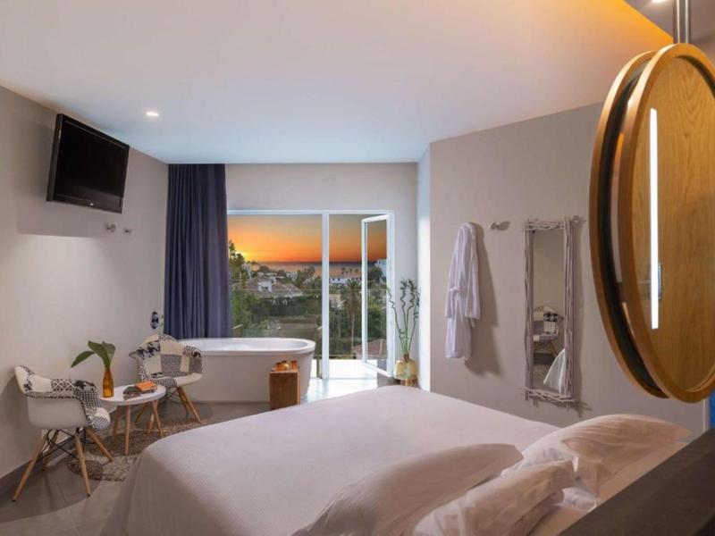 Modernes Hotelzimmer mit großem Bett, Schreibtisch, TV und Blick auf den Sonnenuntergang.