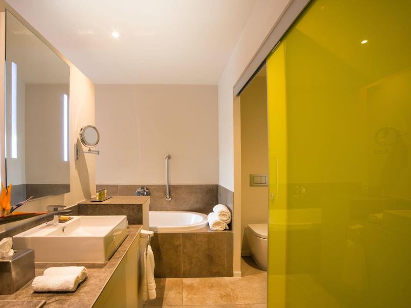 Modernes Badezimmer mit Wanne, Waschbecken, großem Spiegel und gelber Glastür