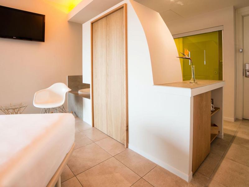 Modernes Hotelzimmer mit Bett, Stuhl, Fernseher und Schrank mit gebogenem Abschluss.