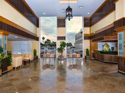 Großer heller Lobbybereich mit Marmorboden, Holzakzenten, Pflanzen und moderner Deckenbeleuchtung.