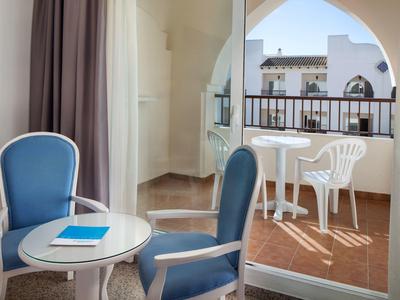 Hell eingerichteter Balkon mit weißem Plastikstuhl und Tisch, davor zwei blaue Sessel und ein kleiner runder Tisch.