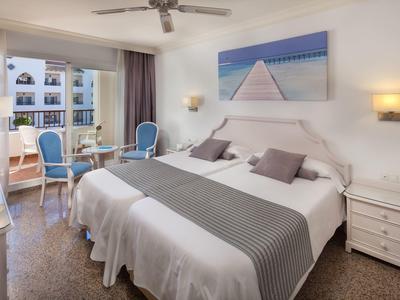 Modernes Hotelzimmer mit Doppelbett, Sitzbereich, Ventilator und großem Meeresbild an der Wand.