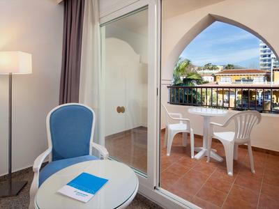 Gemütlicher Balkon mit weißem Tisch und Stühlen, verbunden mit modernem Zimmer und blauem Sessel.