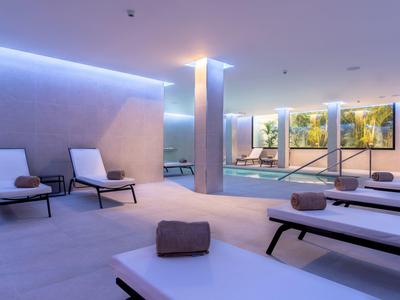 Moderner Wellnessbereich mit Liegen, Handtüchern, Schwimmbad und ruhiger Beleuchtung.