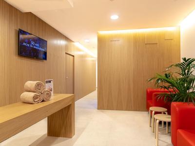 Heller Warteraum mit roten Sitzbänken, Holzvertäfelung, TV und grüner Pflanze.