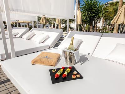 Weißes Sonnendeck mit Kissen, Obst-Spießen auf schwarzem Teller, Champagnerflasche in Eisbehälter.