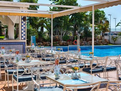 Terrasse mit zwei Liegestühlen, geschlossenem Sonnenschirm und weißen Wänden, blauem Himmel.