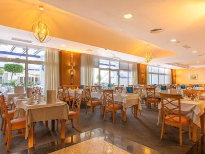 Großes, helles Restaurant mit Holzstühlen, gedeckten Tischen und großem Fensterfrontbereich.