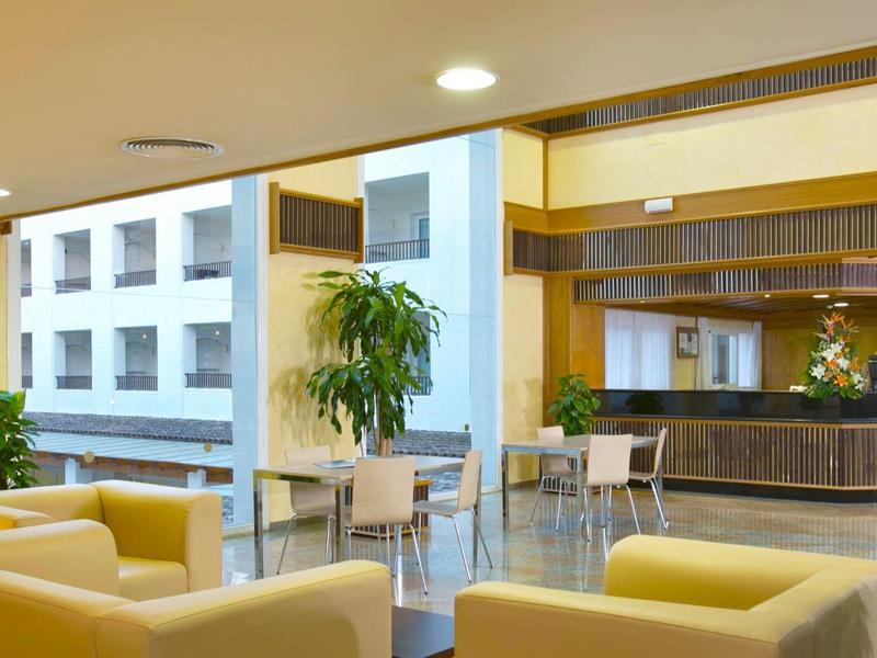 Modern eingerichteter Raum mit hellen Sesseln, Pflanzen und großer Theke aus Holz und Glas.