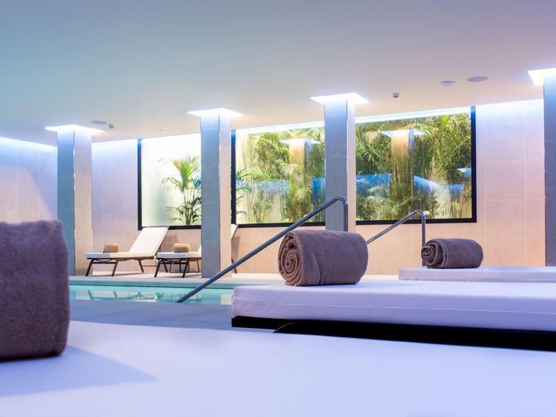 Moderner Wellnessbereich mit Pool, Liegen, großen Fenstern und sanfter Beleuchtung.