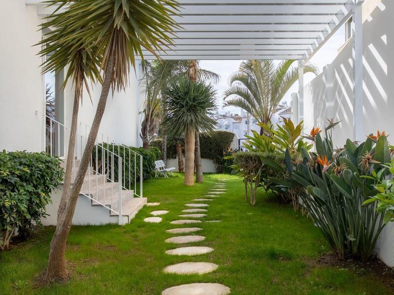 Grüner Garten mit runden Steinen als Weg, Palmen und modernen weißen Gebäuden bei blauem Himmel.