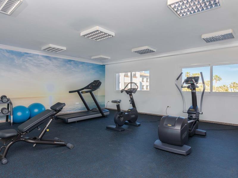 Kleiner Fitnessraum mit Laufbändern, Fahrrad, Hanteln und blauer Gymnastikmatte, weiße Wände.