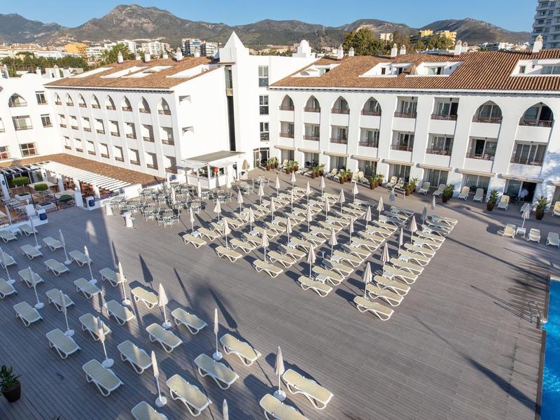 Großer Hotelpoolbereich mit Reihen von Liegestühlen und weißen Sonnenschirmen unter klarem Himmel.