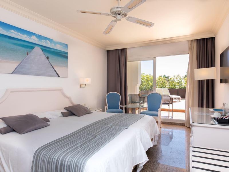 Helles Schlafzimmer mit Doppelbett, blau-weißen Stühlen, Balkon und Gartenblick.