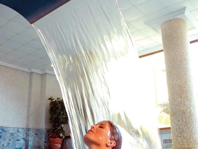 Ein Garten mit Palmen, gelben Gebäuden und steinigen Gehwegen unter blauem Himmel.