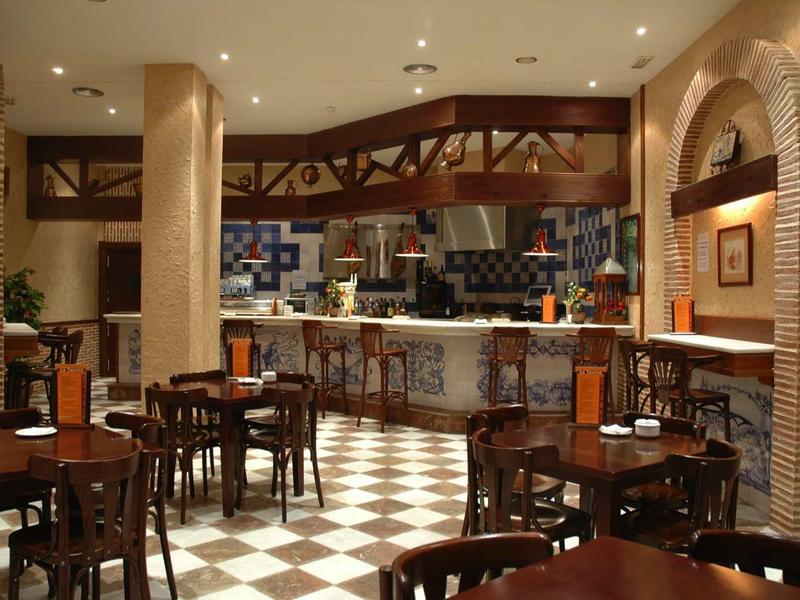 Innenraum eines Restaurants mit Holzstühlen, Tischen und einem Barbereich, gemusterter Fliesenboden.