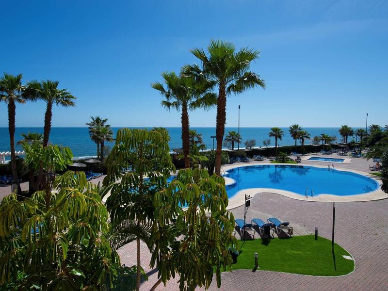 Poolanlage mit Palmen und Blick auf das blaue Meer unter klarem Himmel.