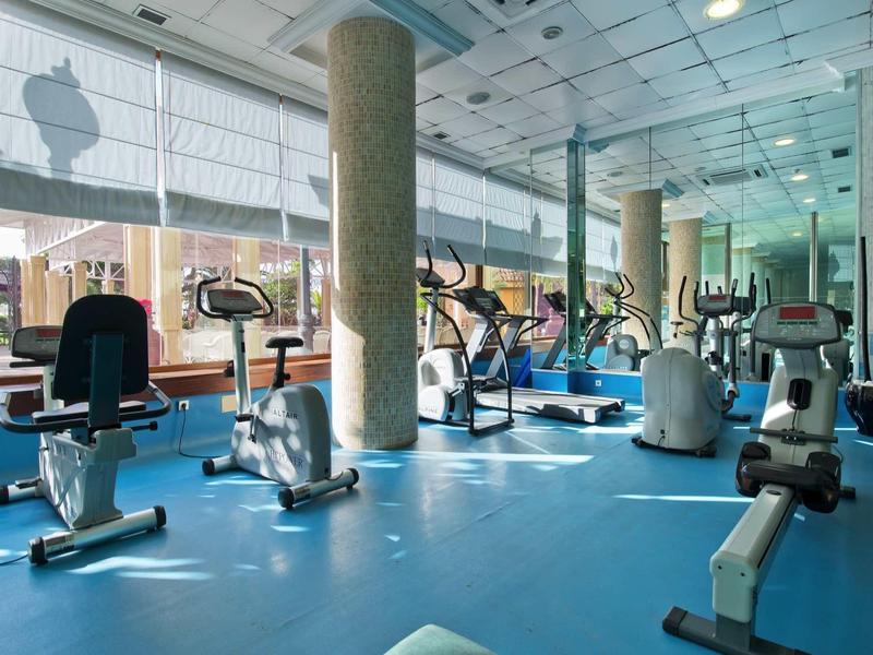 Großer Fitnessraum mit blauen Boden, mehreren Trainingsgeräten und großen Fensterfronten.