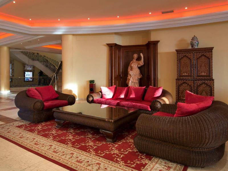 Elegantes Wohnzimmer mit runden Korbsesseln, rotem Teppich und skulpturgeschmücktem Holzmöbel.