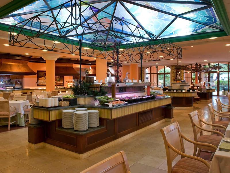 Großes, helles Buffet-Restaurant mit vielen Tischen, Stühlen und einem farbigen Glaskuppel-Dach.