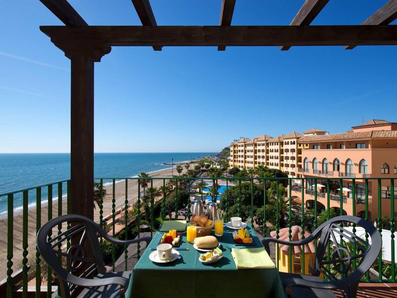 Meerblick von Balkon mit grün gedecktem Tisch, Stühlen und Blick auf Hotelanlage und Pool.