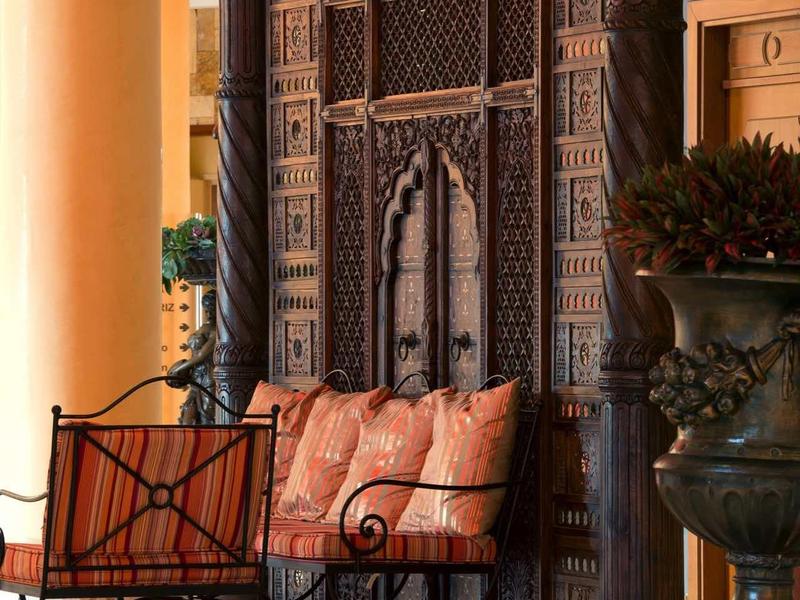 Antikes, kunstvoll verziertes hölzernes Tor mit Sitzbank und rosa Kissen davor in hellem Raum.