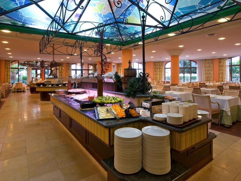 Ein heller, großer Speisesaal mit Buffet und vielen gedeckten Tischen, bunte Deckenmalerei sichtbar.