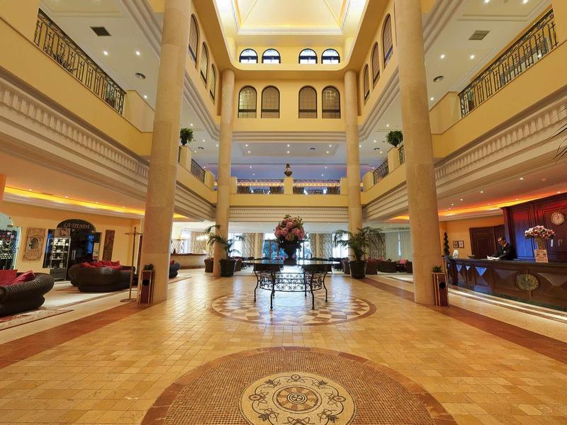Großer Hotellobby mit hohen Säulen, goldener Beleuchtung und zentralem Blumenarrangement.