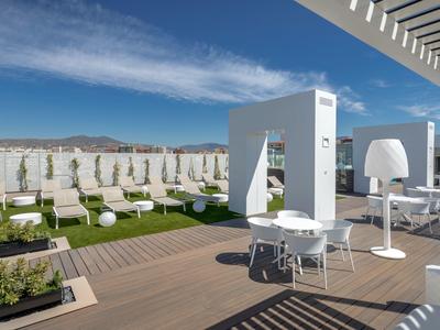 Modernes Außendeck mit weißen Tischen, Stühlen, Sonnenschirmen und grüner Wiese bei klarem Himmel.