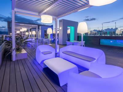 Moderne Dachterrasse mit blauer LED-Beleuchtung, weißen Sitzmöbeln und Holzboden bei Dämmerung.