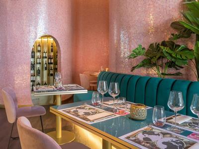 Modern eingerichteter Gastronomiebereich mit türkisfarbenem Sofa, runden Stühlen und rosafarbenen Wänden.