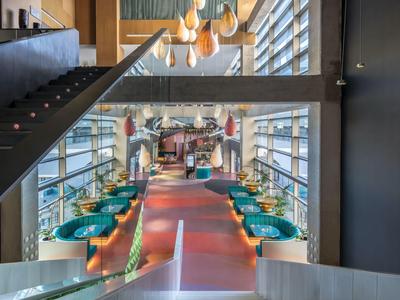 Moderner Hotelrestaurant-Innenraum mit bunten Sesseln, großen Fenstern und Treppe.