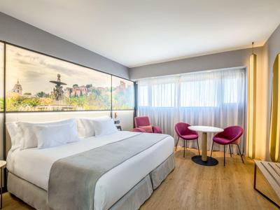 Helles Hotelzimmer mit großem Bett, modernen Möbeln, rotem Sessel und Panoramablick an der Wand.