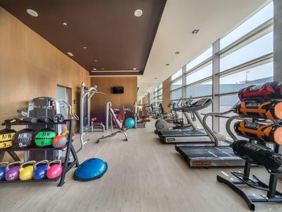 Moderner Fitnessraum mit Trainingsgeräten, Hanteln und großen Fenstern mit Blick nach draußen.