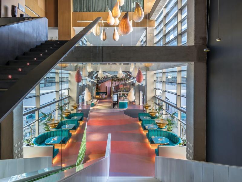 Moderner Hotelrestaurant-Innenraum mit bunten Sesseln, großen Fenstern und Treppe.