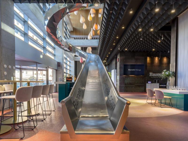 Moderner Hotelbereich mit großer Rutsche, Sitzgelegenheiten und heller Innenraumgestaltung.