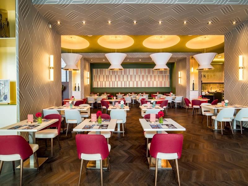 Modernes Restaurant mit roten Stühlen, weißen Tischen und dekorativer Decke.