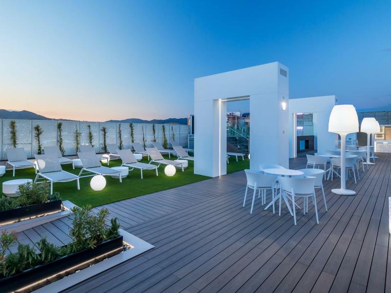 Moderner Dachgarten mit Holzboden, weißen Möbeln und stimmungsvoller Abendbeleuchtung.