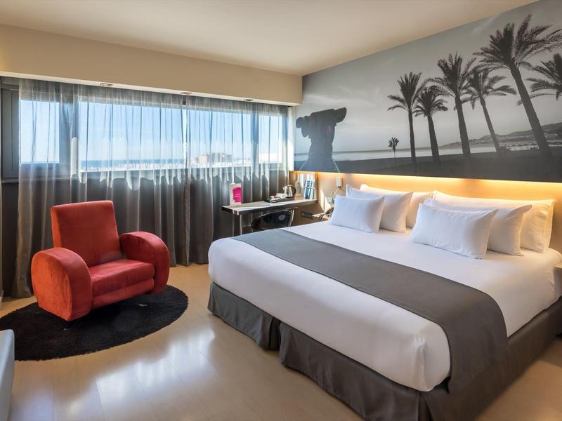 Modern eingerichtetes Schlafzimmer mit rotem Sessel, großem Bett und Palmen-Wandbild.