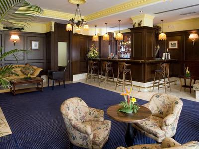 Gemütliche Hotelbar mit dunkelbraunen Holzmöbeln, blauer Teppich und bequemen Sesseln.