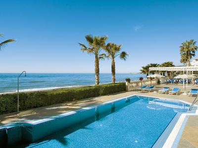 Piscina dell'hotel con vista sul mare, palme e lettini sotto un cielo azzurro limpido.