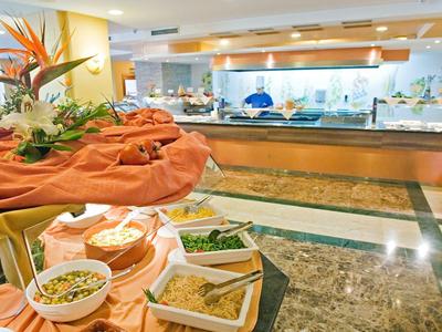 Strand mit Sonnenschirmen und Palmen, ruhiges Meer, Sonnenuntergang, Promenade und Sitzbereiche.