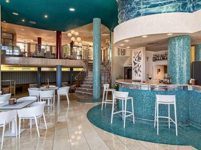 Lobby di hotel moderna con bar, colonne rotonde e aree salotto eleganti.