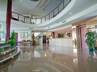 Heller, großzügiger Empfangsbereich mit glänzendem Boden, Pflanzen und runder Treppe.