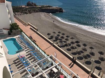 Blick auf einen Strand mit Sonnenschirmen und angrenzendem Hotelpool unter blauem Himmel.