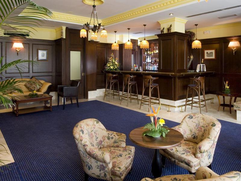 Gemütliche Hotelbar mit dunkelbraunen Holzmöbeln, blauer Teppich und bequemen Sesseln.